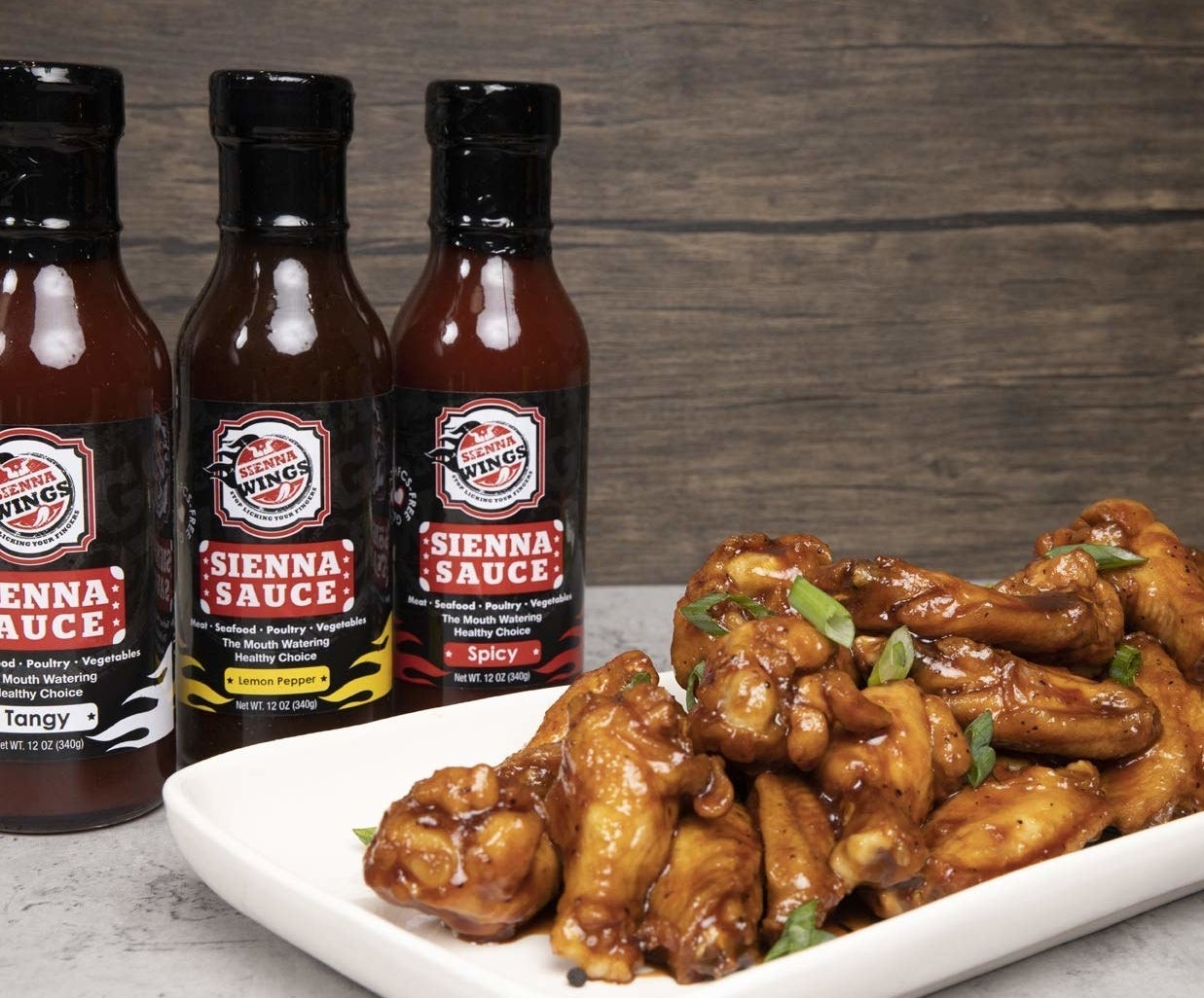 three bottles of Sienna Sauce sitting next to a plate of wings