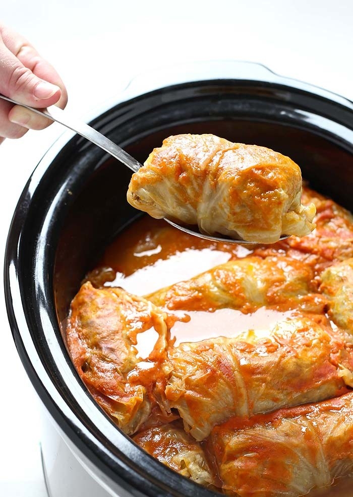 A slow cooker filled with stuffed cabbage rolls in tomato sauce.