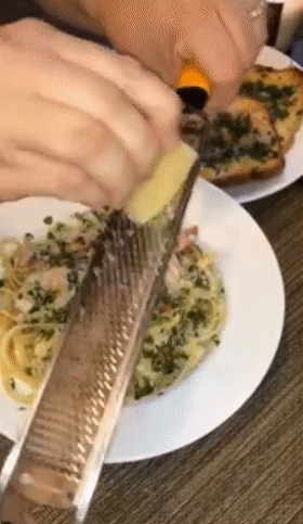 GIF of reviewer using the handheld grater to shave parmesan cheese over a plate of pasta