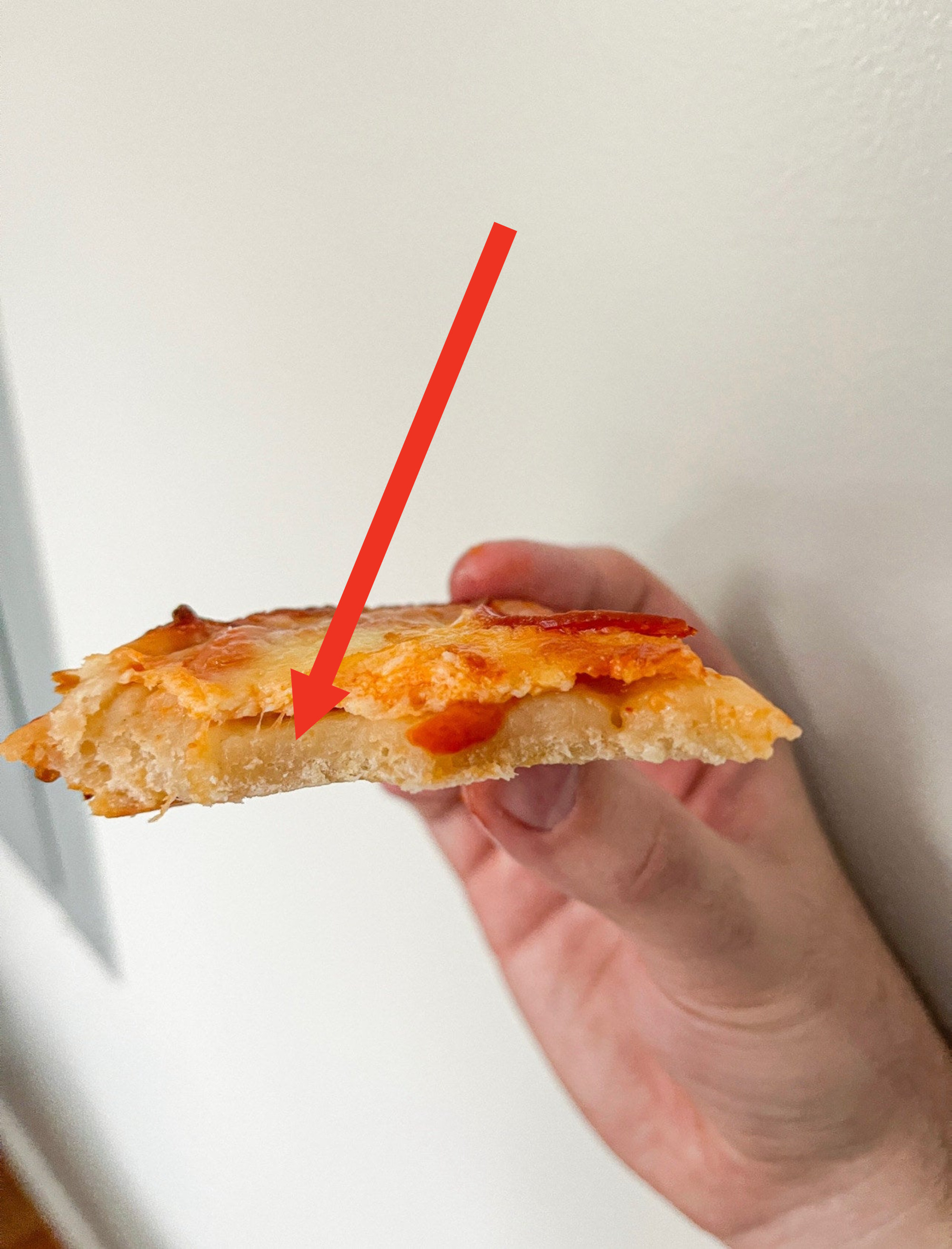 Author holding up slide of pizza with bite taken out of it and revealing a very doughy crust
