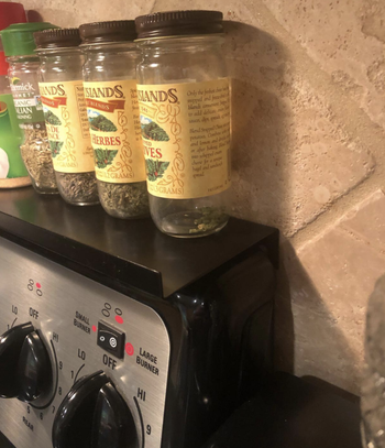 A customer review photo of the shelf holding spices on their stoves ledge