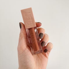 Writer holding up the lip gloss in front of a white wall