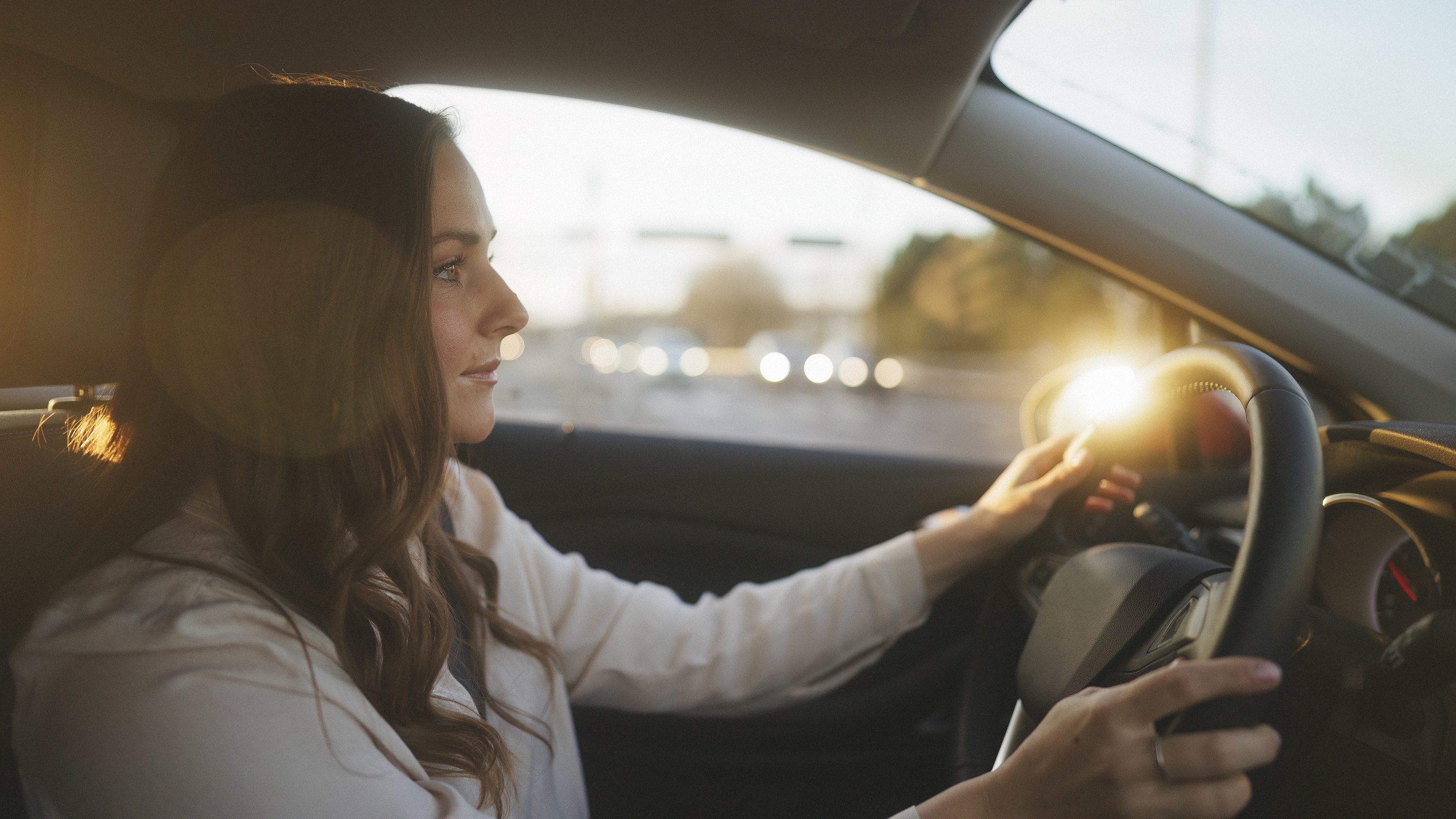 A brunette woman drives her car with golden hour light shining through the window