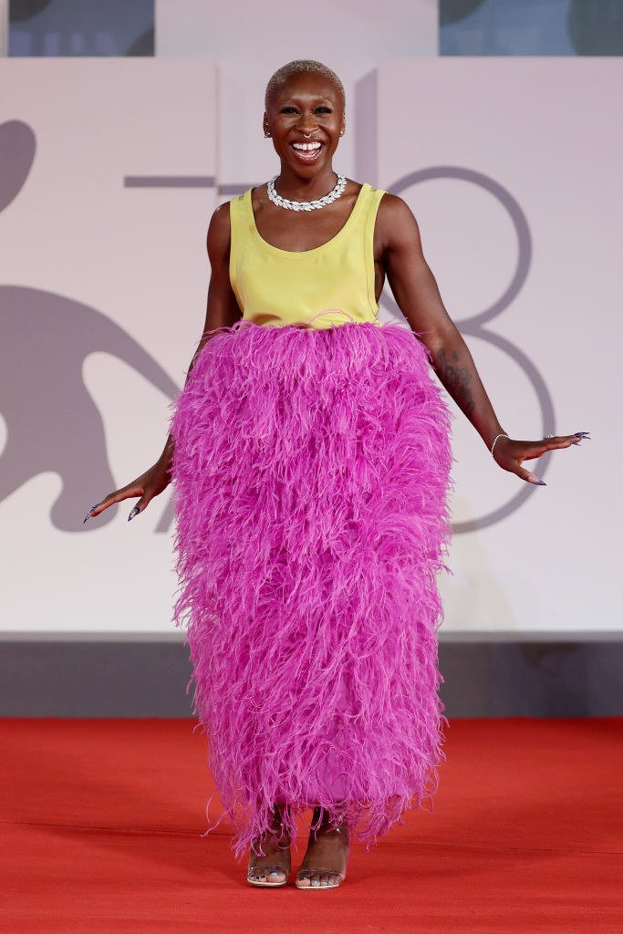 Erivo in tea length dress with yellow bodice and pink feather skirt