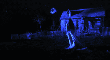 A woman in white walks toward a barn at night
