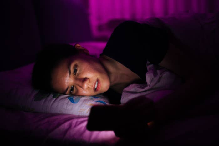 A woman laying in bed at night looking at her phone