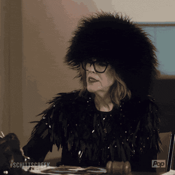 Moira played by Catherine O&#x27;Hara clapping while wearing a fuzzy black hat