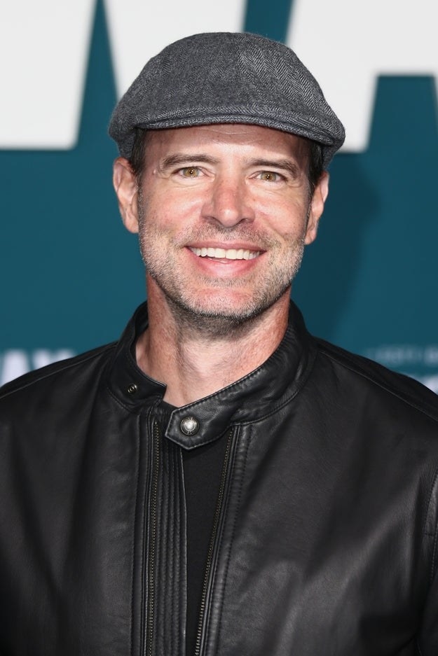 Scott Foley wearing a newsboy hat and leather jacket while posing at an event