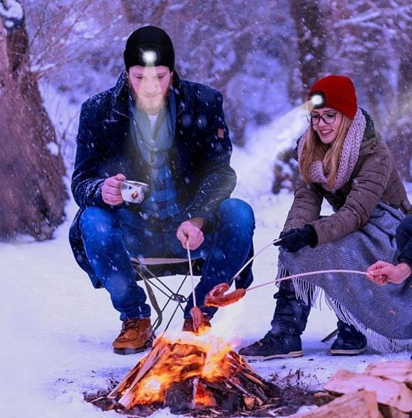 Two people wearing the light up beanie sitting around a campfire at night