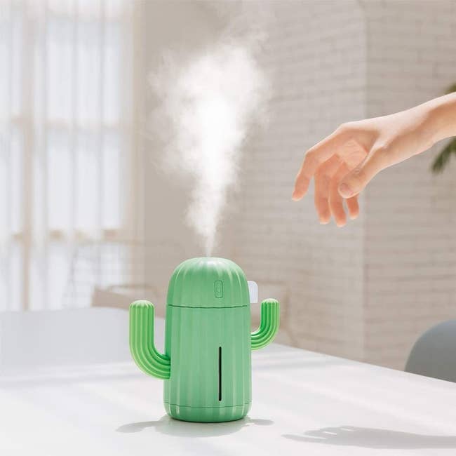 a green humidifier with two arms that looks like a cactus with steam coming out of it