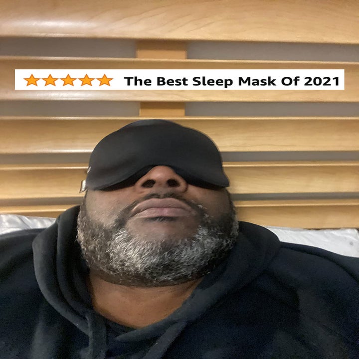 A reviewer in the black sleep mask with text best sleep mask oof 2021