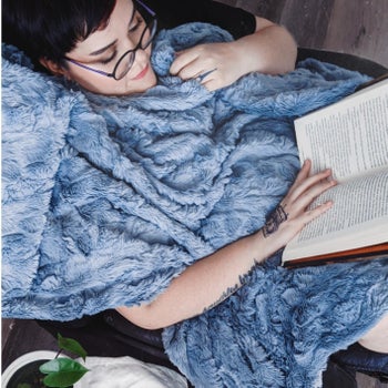 reviewer reading a book while curled up under the blue blanket