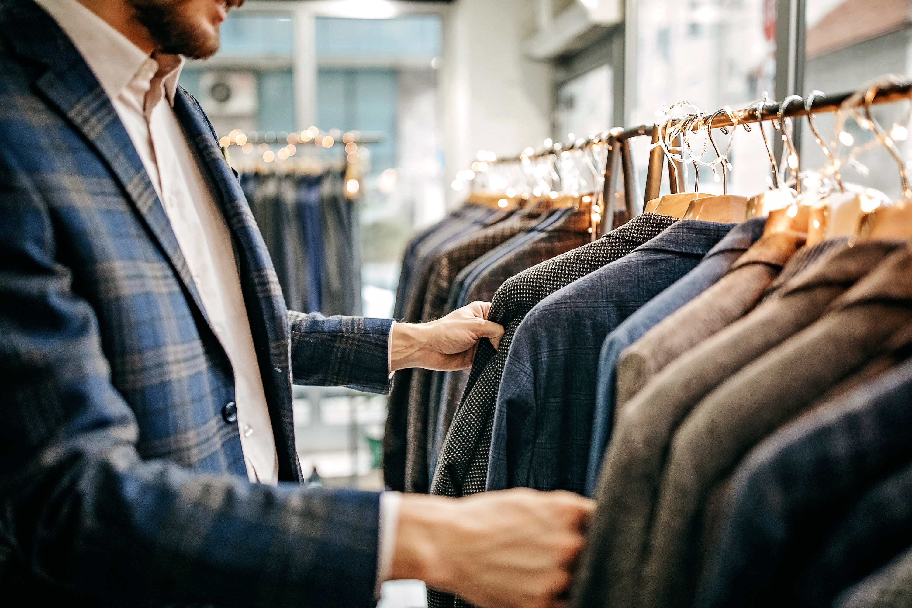 A man in a striped suit looking at suits on hangers in a store