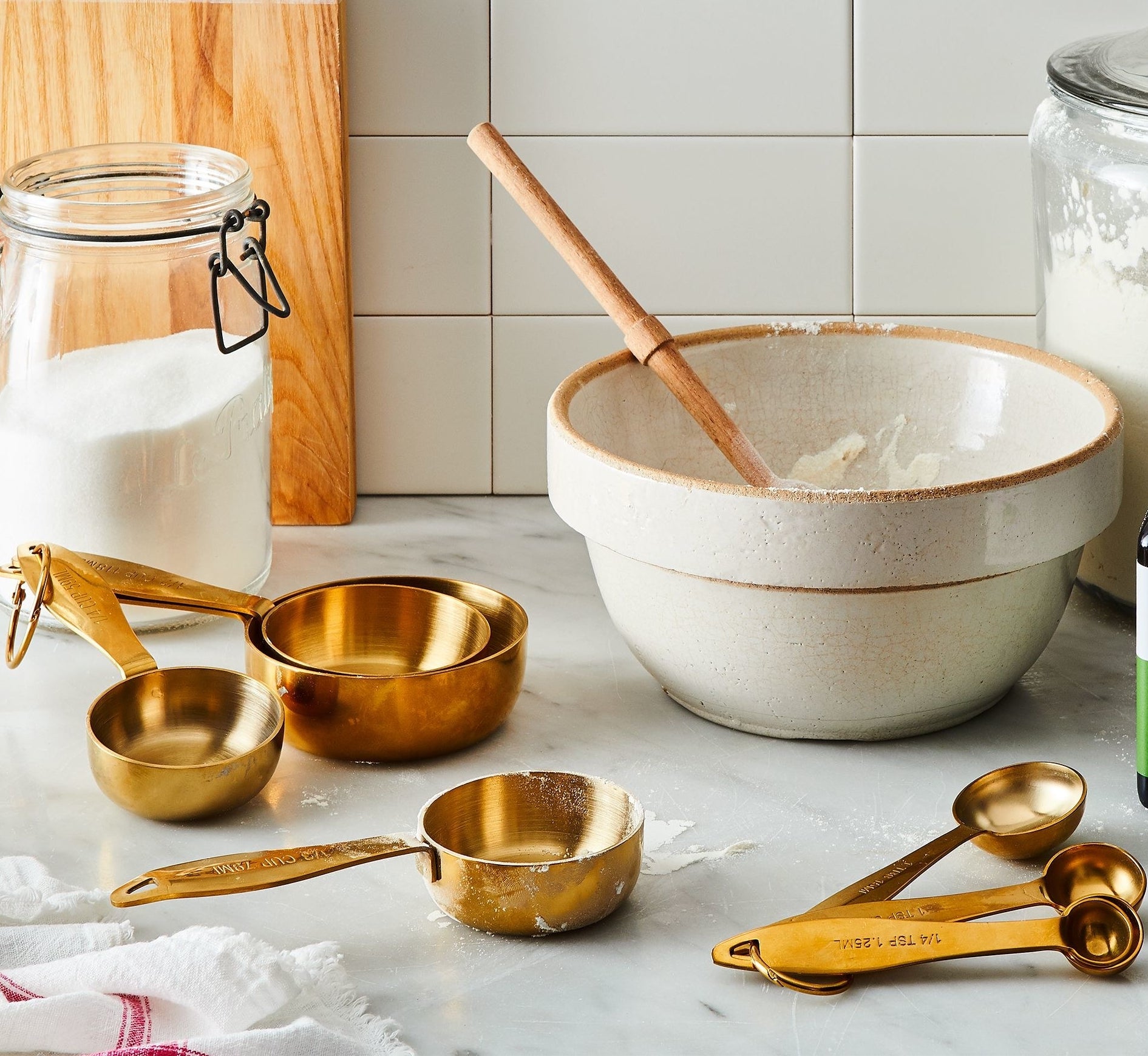 the gold measuring cups and spoons on a counter next to a mixing bowl and baking ingredients