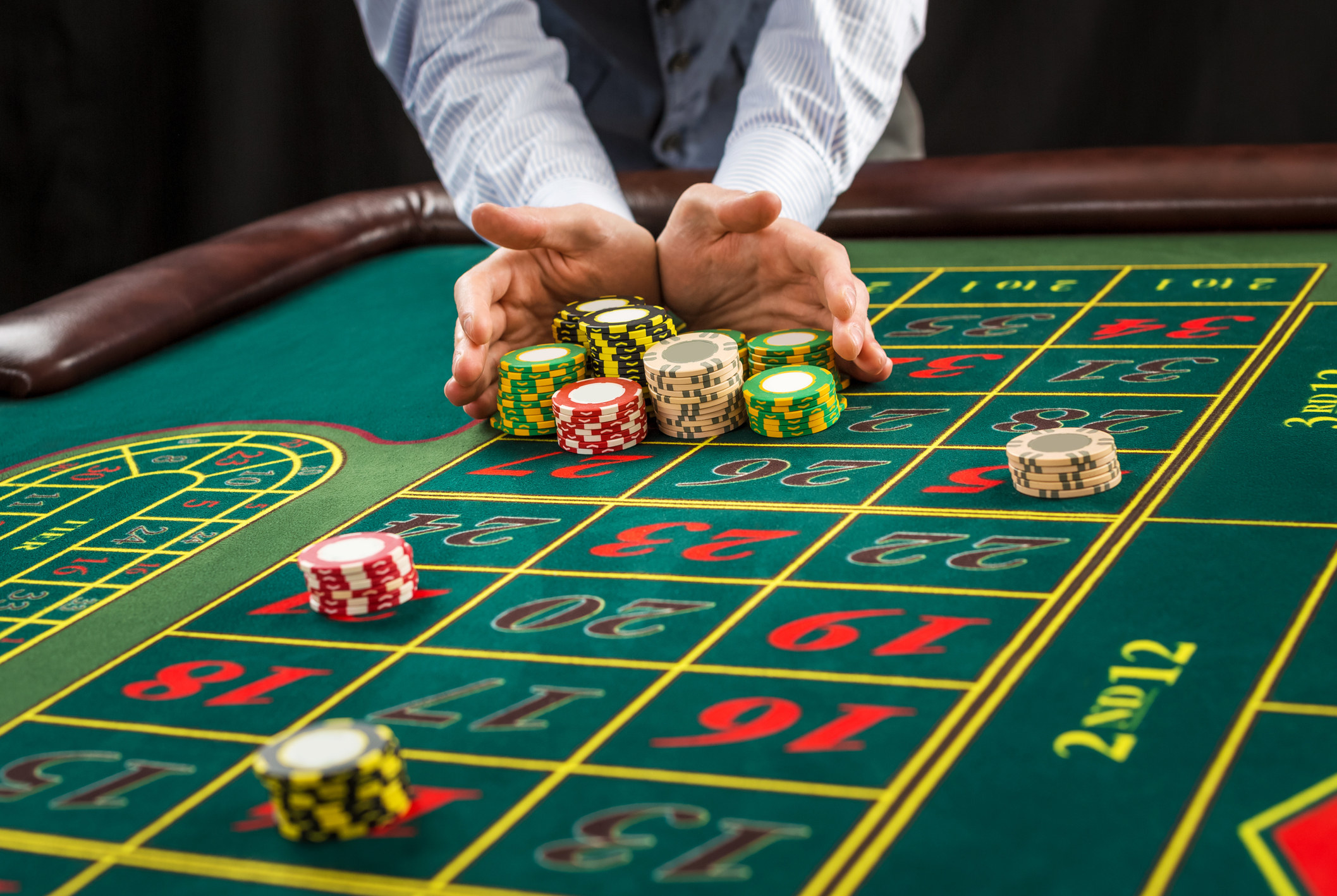 Picture of a green table with betting with chips. Man handing over casino chips.