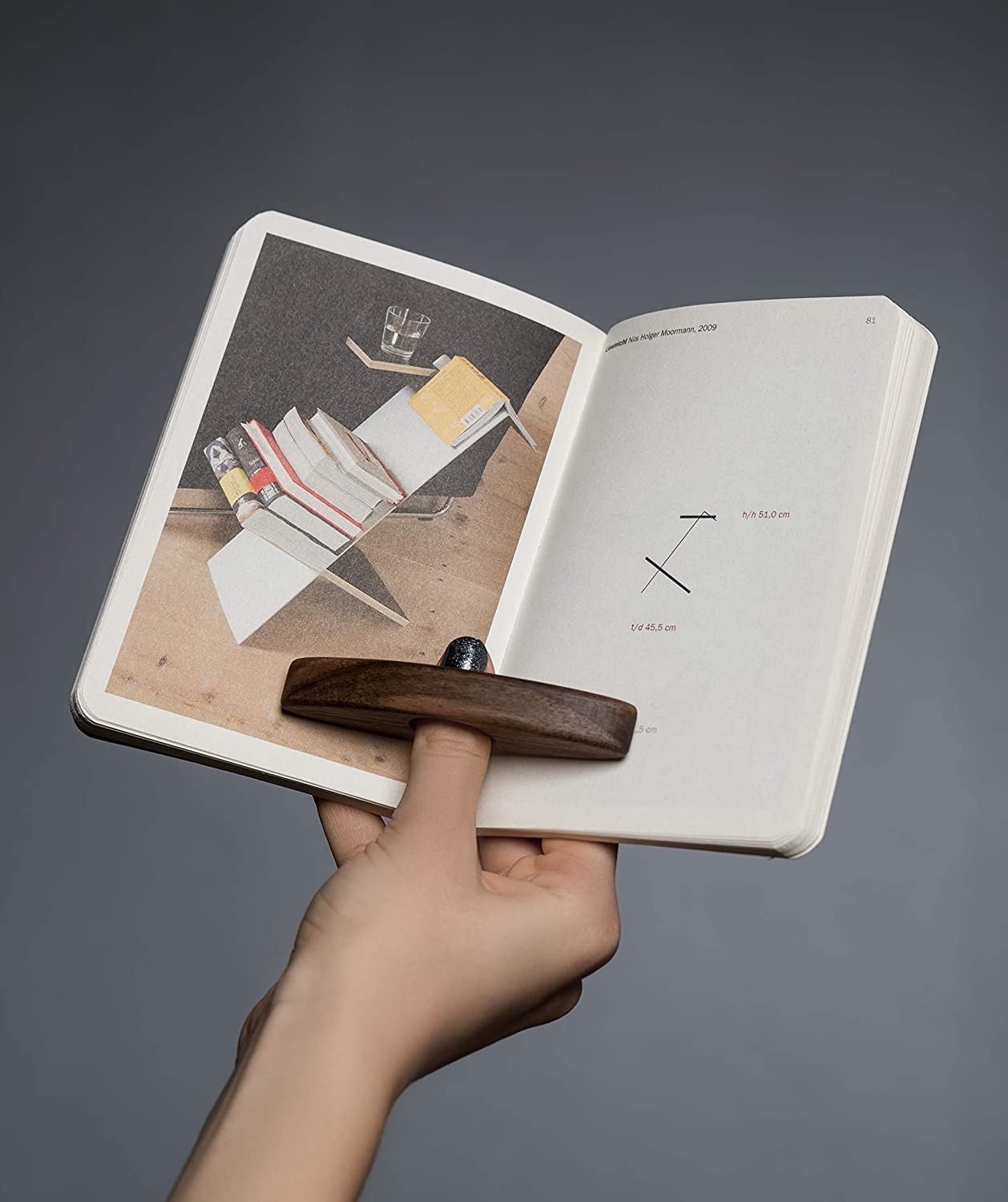 A person&#x27;s hand holding up a book propped open with the thumb gadget