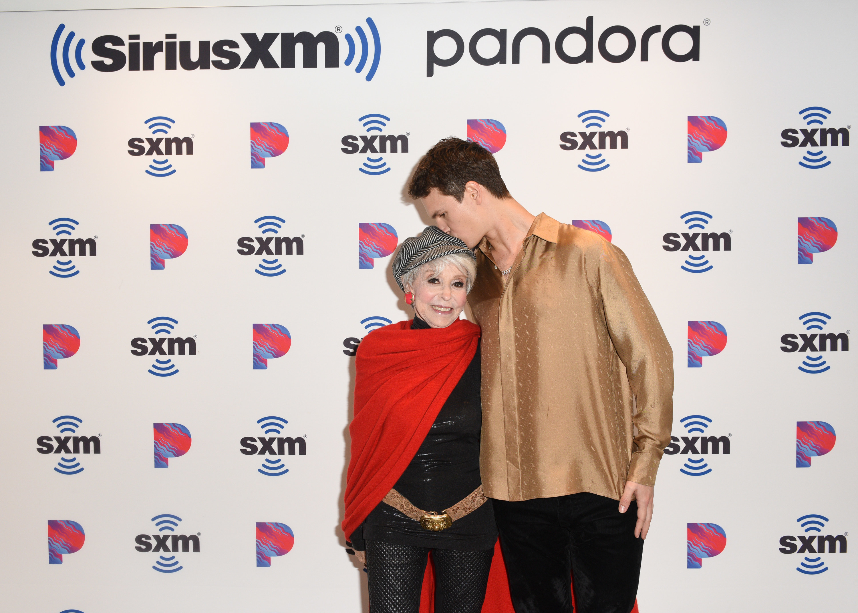 Rita being embraced and kissed on the head by Ansel as they pose for photographers at a red carpet event