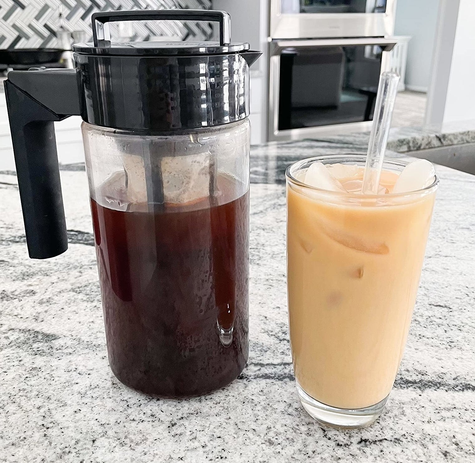 reviewer photo of the black cold brew maker next to a glass of iced cold brew