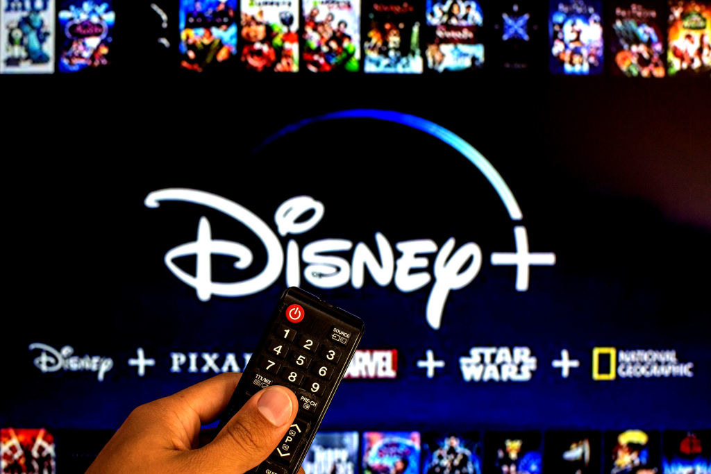 Close-up of a hand holding a TV remote control seen displayed in front of the Disney+ log