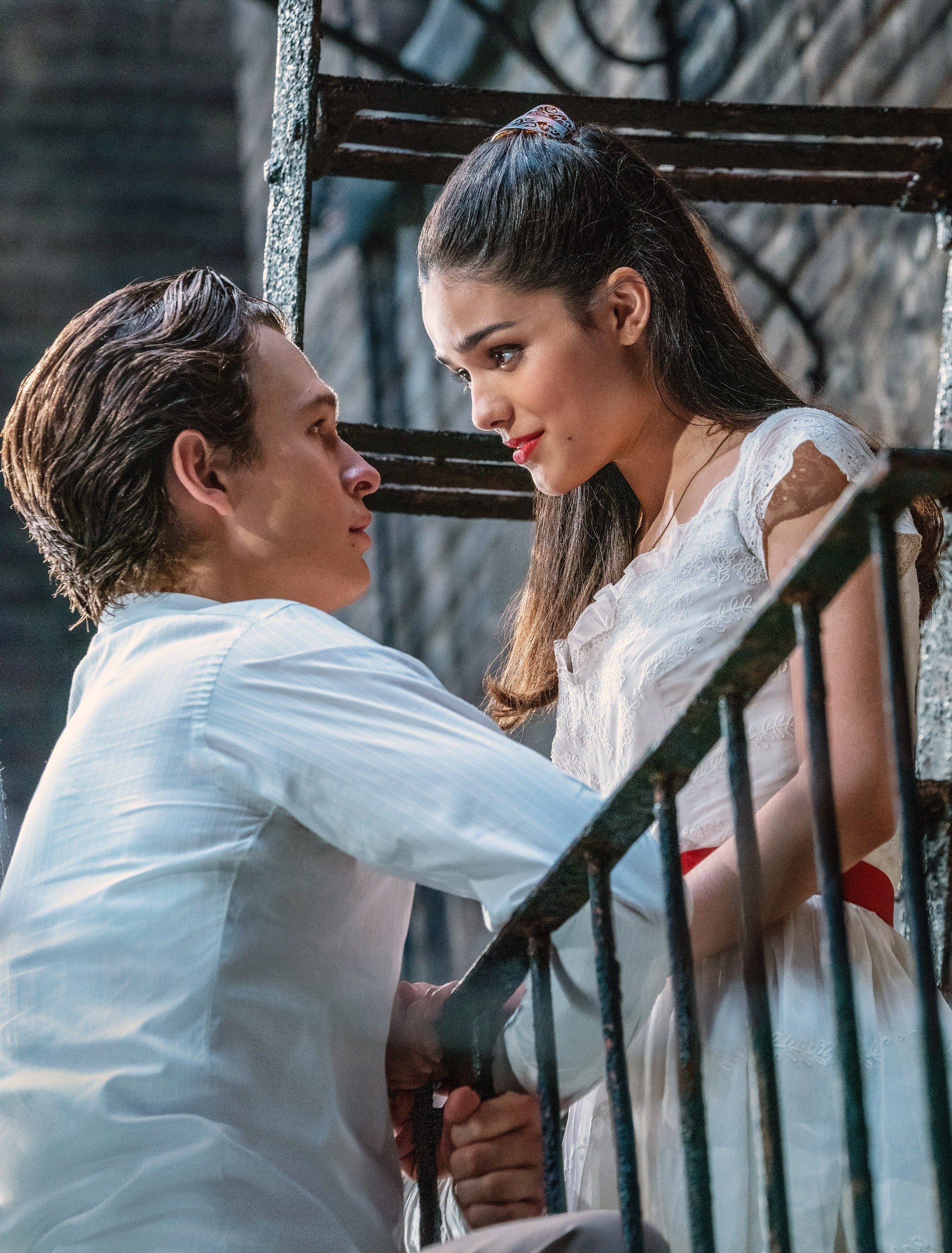 Ansel looking up at Rachel Zegler as they stand on opposite sides of a fire escape in a scene from the film