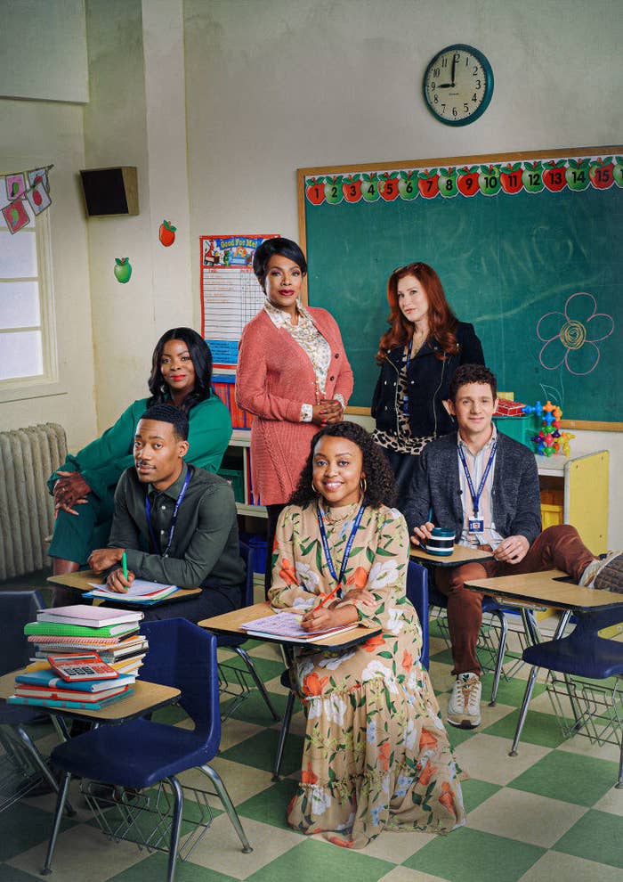 A promo photo of the cast sitting in desks in a classroom