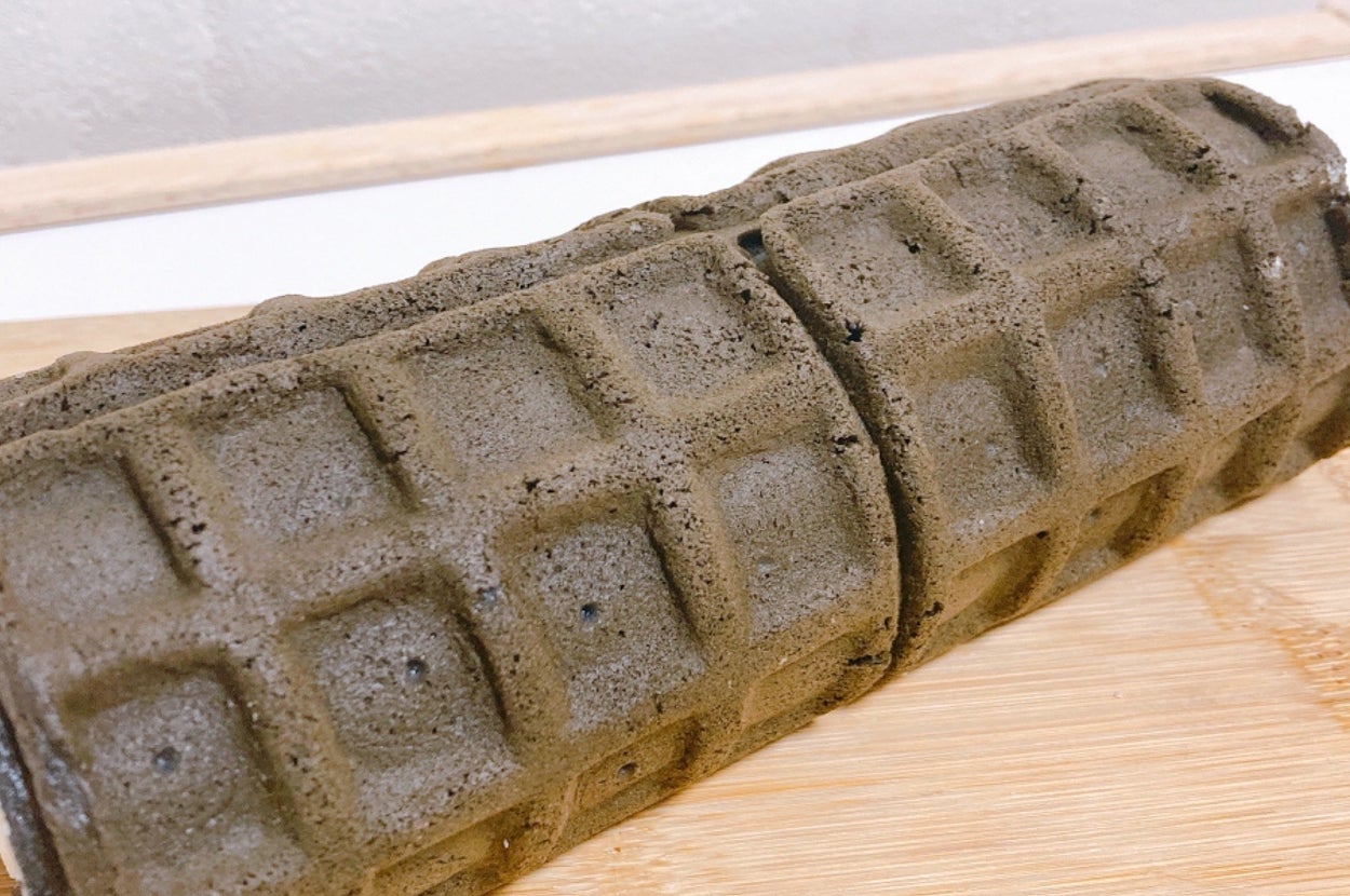 ワッフルの形をした黒いロールケーキが木のプレート上に置かれています。