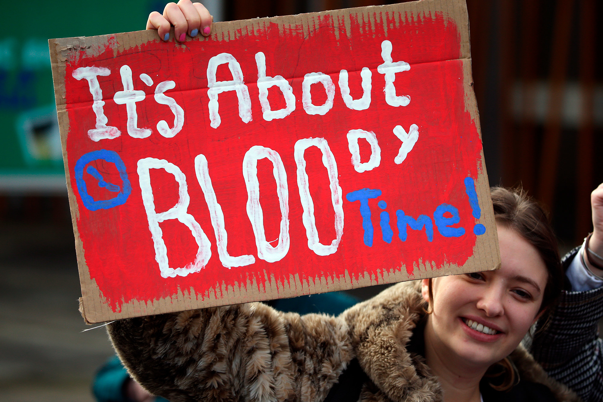 A woman holding up a sign that says &quot;It&#x27;s about bloody time&quot;