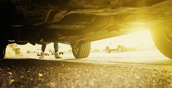 The undercarriage of a car with a pair of legs at the rear of the vehicle