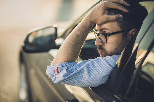 Young man with his hand in his head outside the car window looking worried