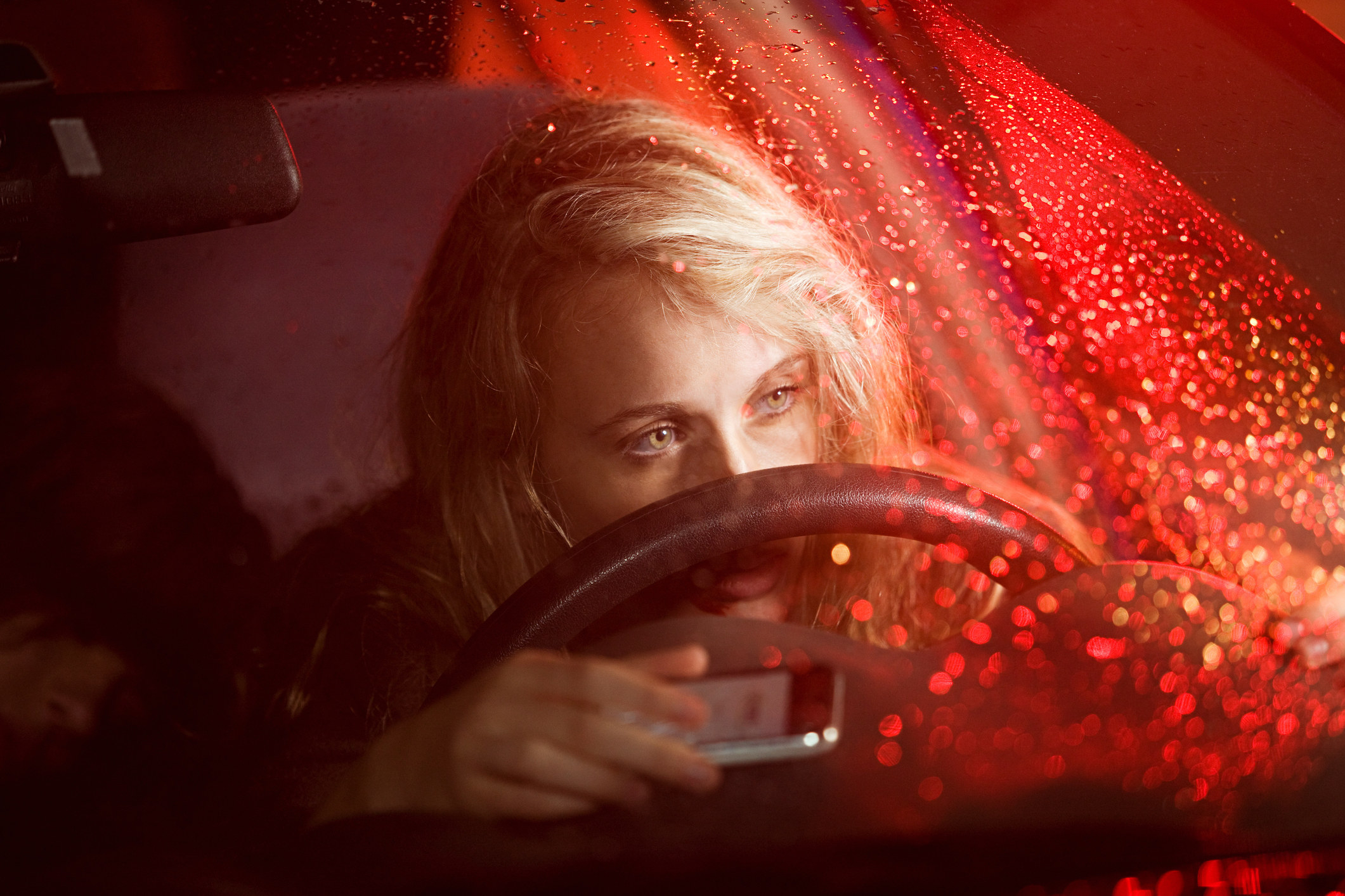 Young woman staring into space behind the wheel of a car with her nose resting on the wheel
