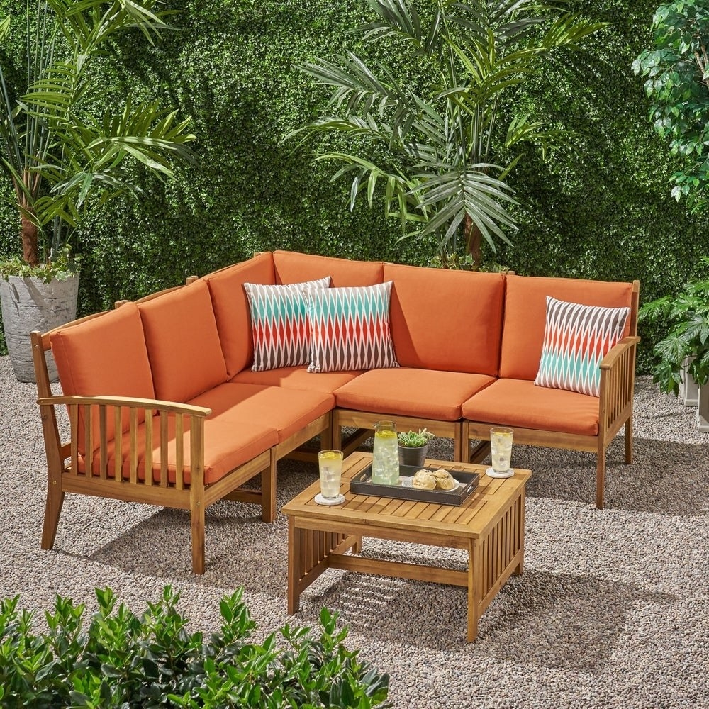 wooden L-shaped sectional with orange cushions in an outdoor leafy patio