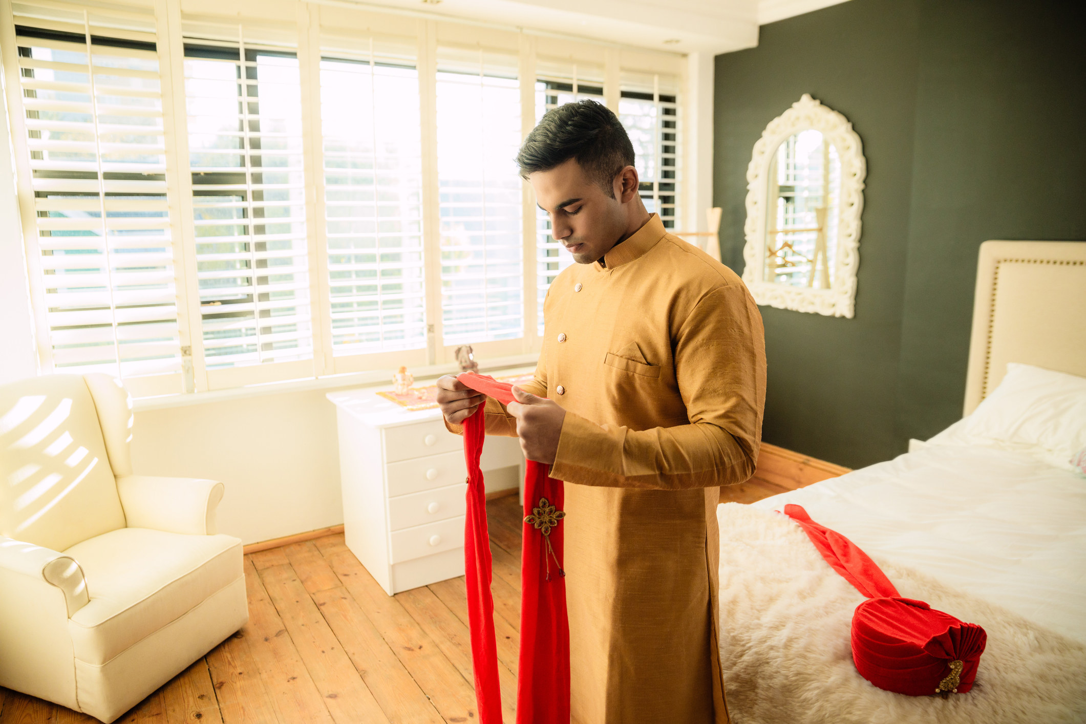 Young groom getting dressed on his wedding day in a traditional Indian wedding outfit