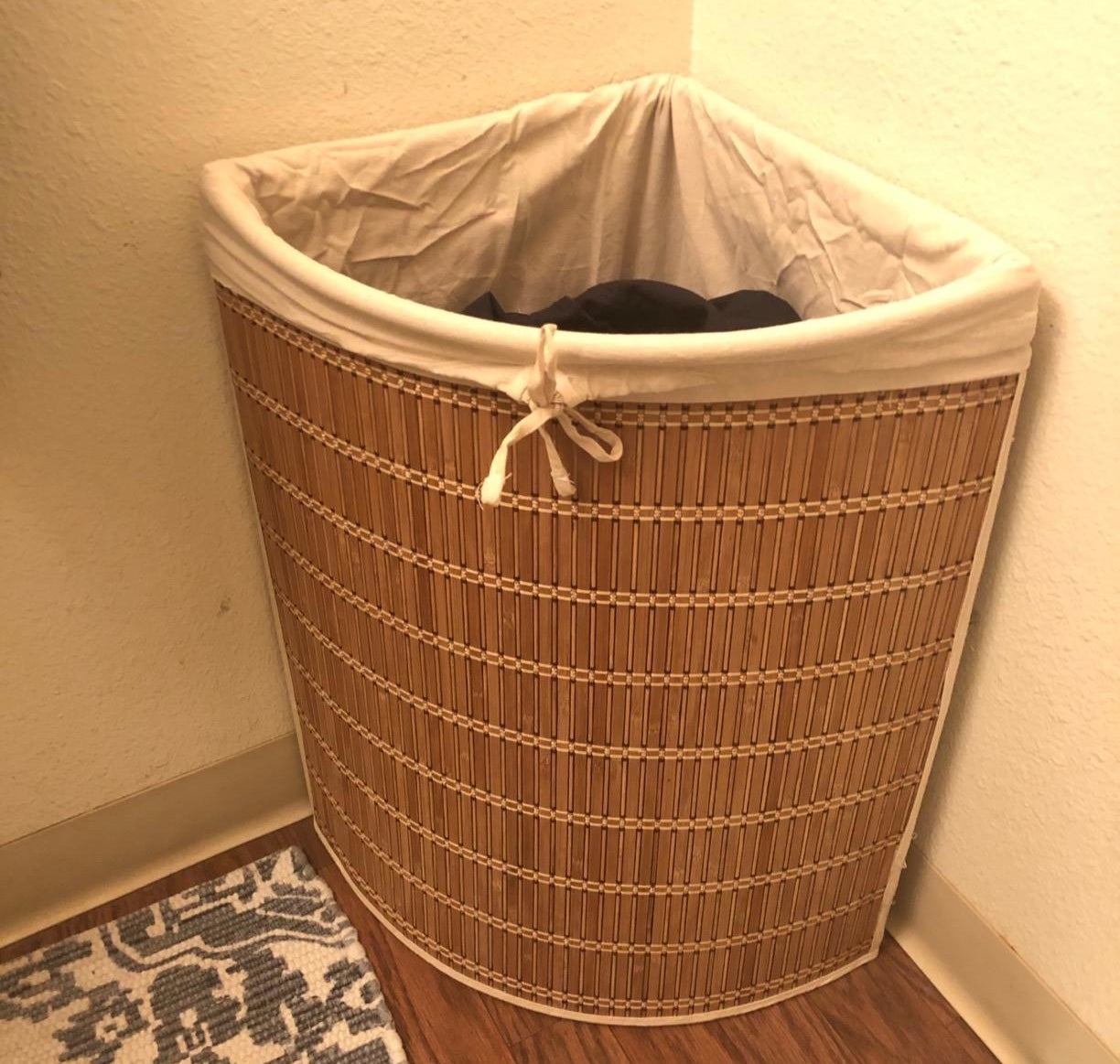 a reviewer photo of the hamper in the corner of a room with clothes inside