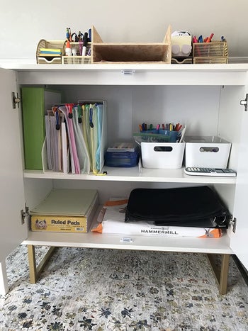 reviewer photo of the inside of the accent table showing two shelves filled with files, pens, paper, and other office supplies