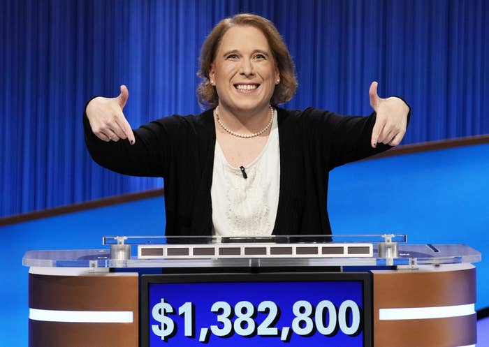 A contestant on the game show Jeopardy grins and points down at a sign reading how much money she won, $1,382,800