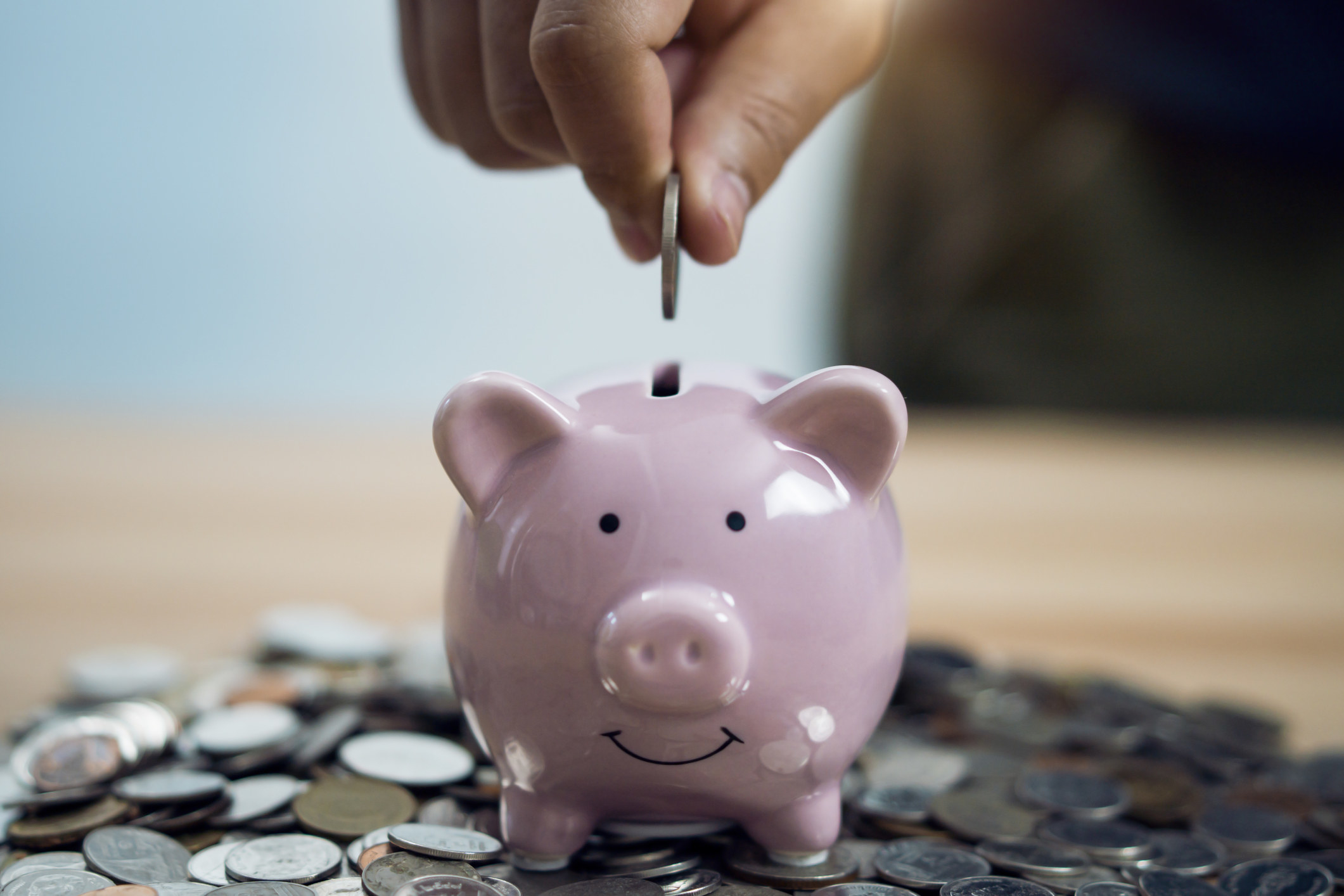 Person putting coin in piggy bank at table