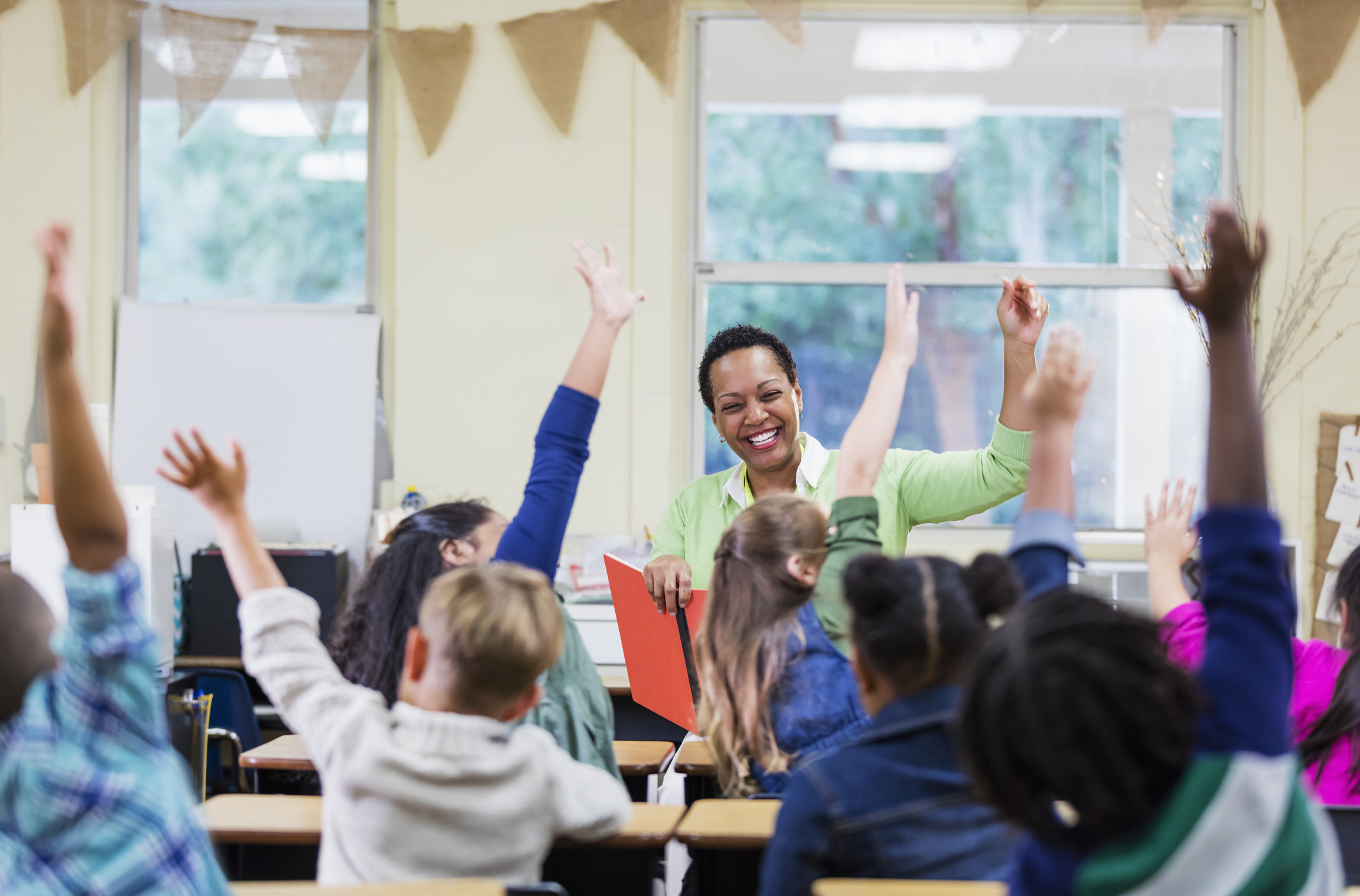 A stock image of a teacher smiling as she and her students wave their hands