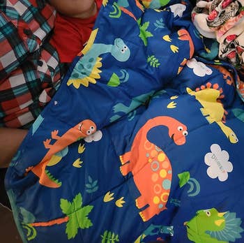 reviewer's photo of their child sleeping under the blue dinosaur print blanket