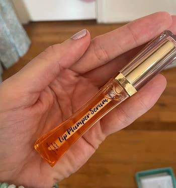 Reviewer holding gold and orange tube of lip plumper