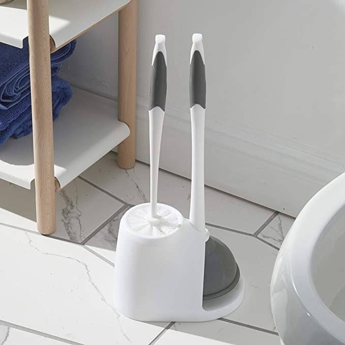 The plunger and brush combo sitting in a holder on a bathroom floor