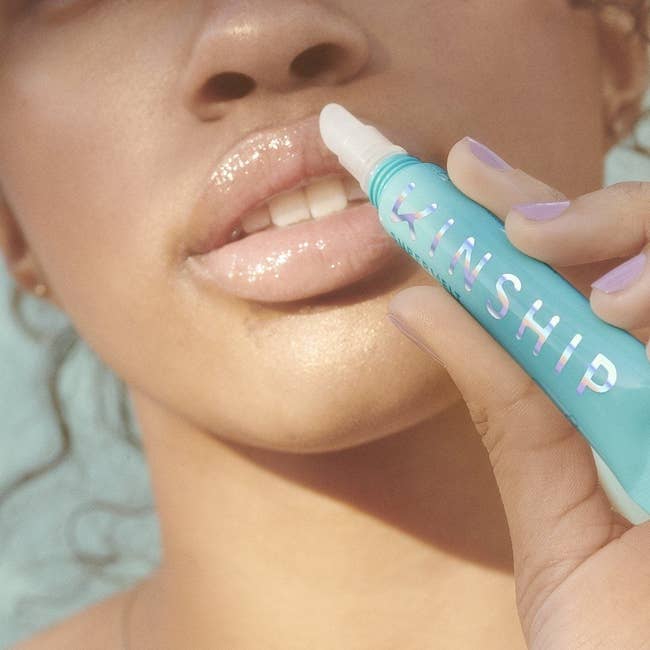 Model applying blue tube of lip plumper to lips
