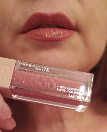 Reviewer holding dark pink tube of lip gloss below lips