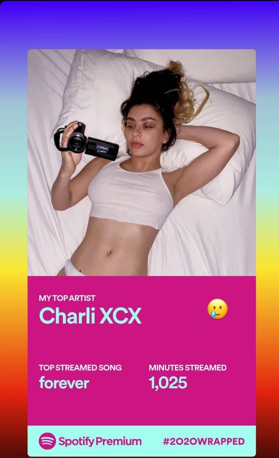 A screenshot from Spotify that reads "My top artist: Charli XCX." In the photo, Charli is lying down holding a video camera and wearing a cropped shirt