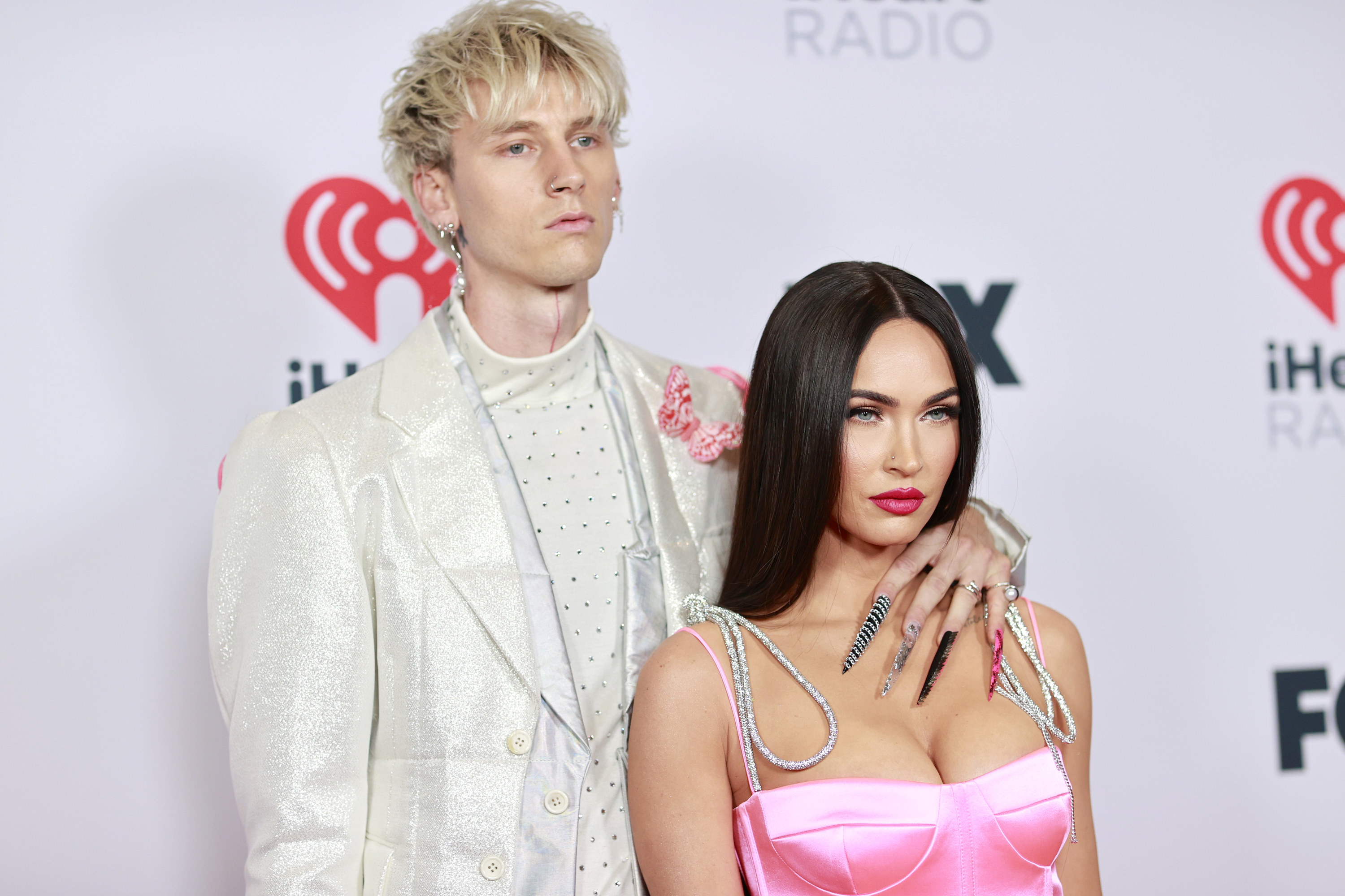 MGK with his arm around Megan as they pose on the red carpet for an I heart radio event