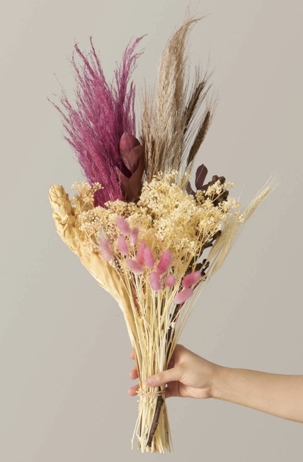 a person holding the cream and mauve dried bouquet