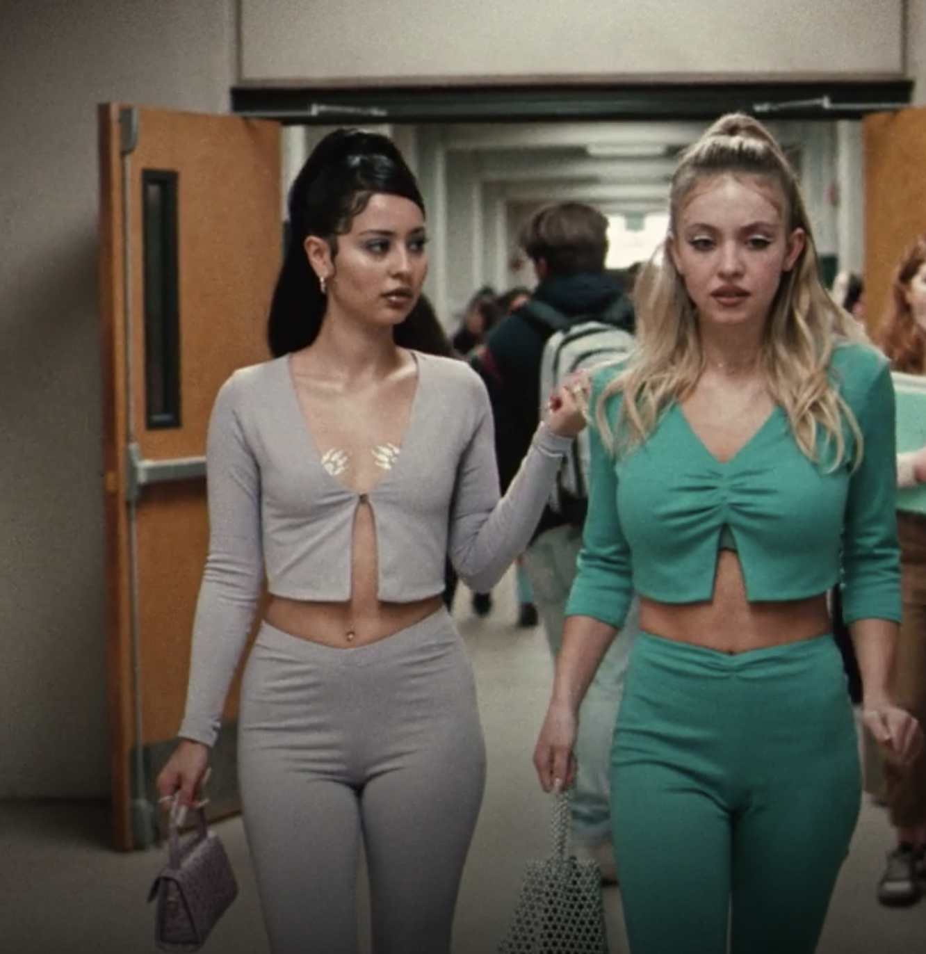 Maddy and Cassie walking down the hallway of their school wearing similar knit long-sleeved crop tops and pants