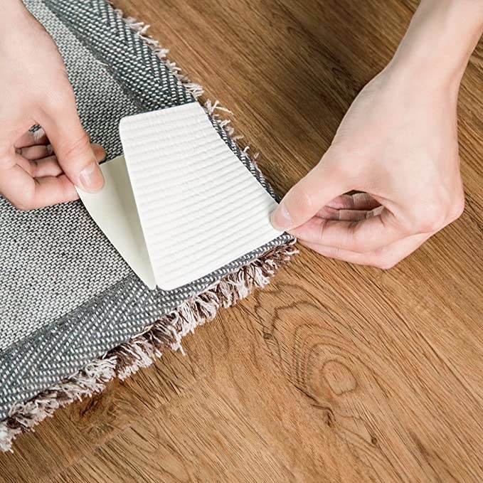 A person sticking a grip to the bottom of a rug