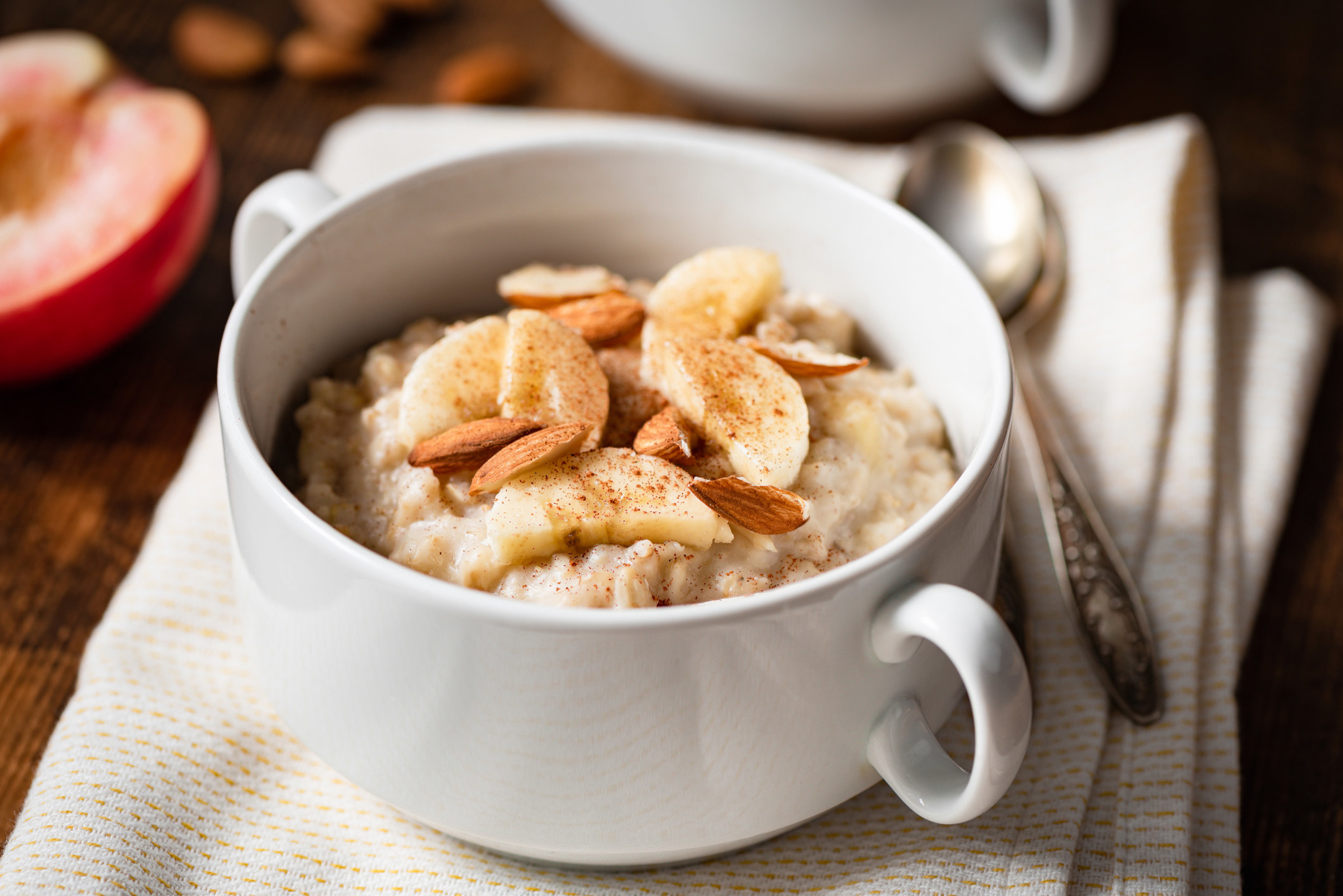 Oatmeal porridge with banana, cinnamon, and almonds in a white bowl. Healthy breakfast food.