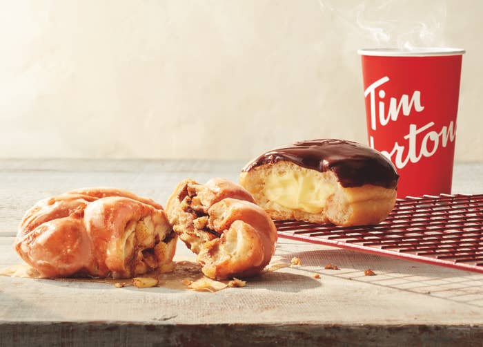 A photo of three donuts on a table with a Tim Horton&#x27;s coffee behind