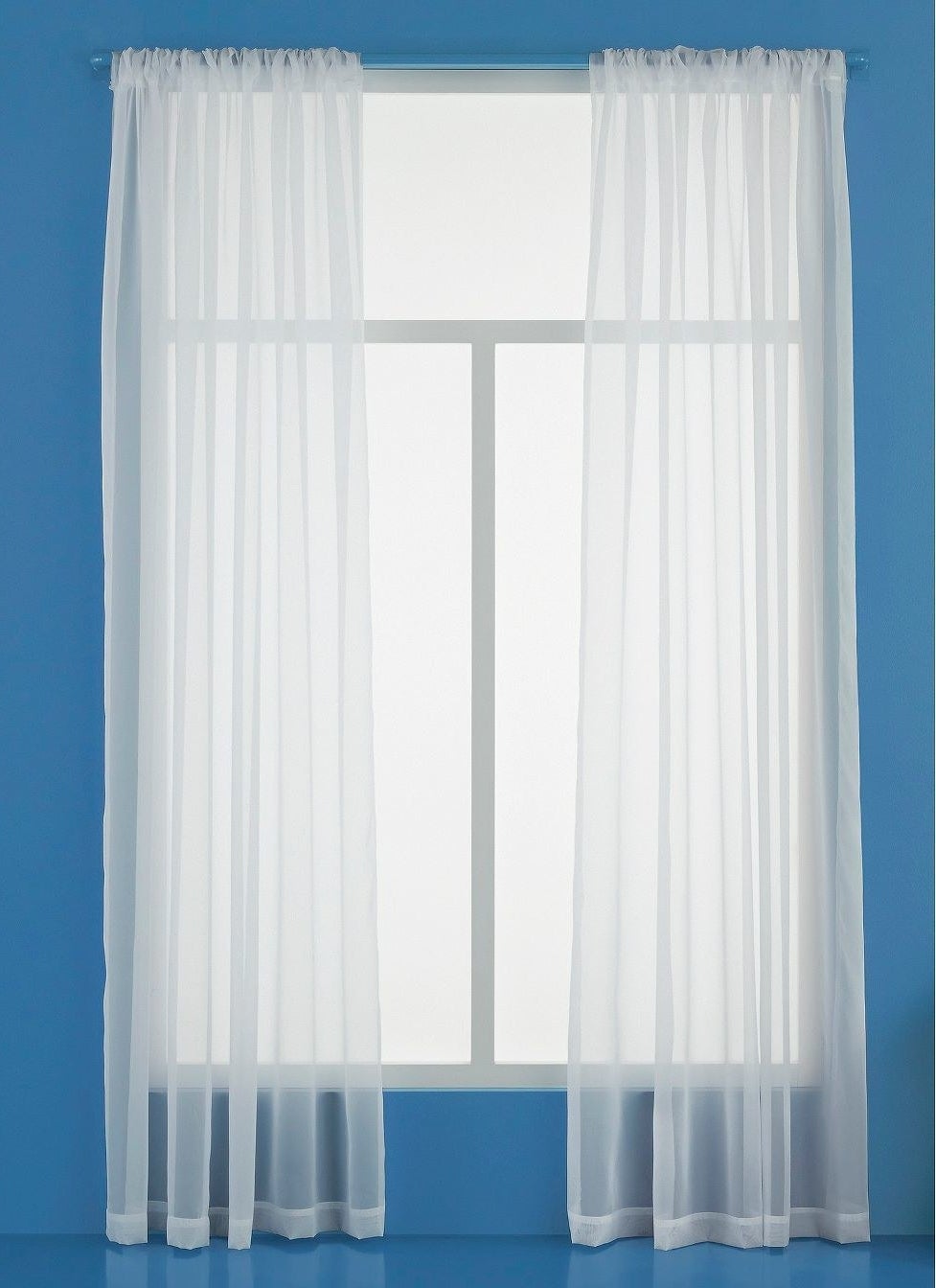 A set of sheer white curtains on a window in a blue room